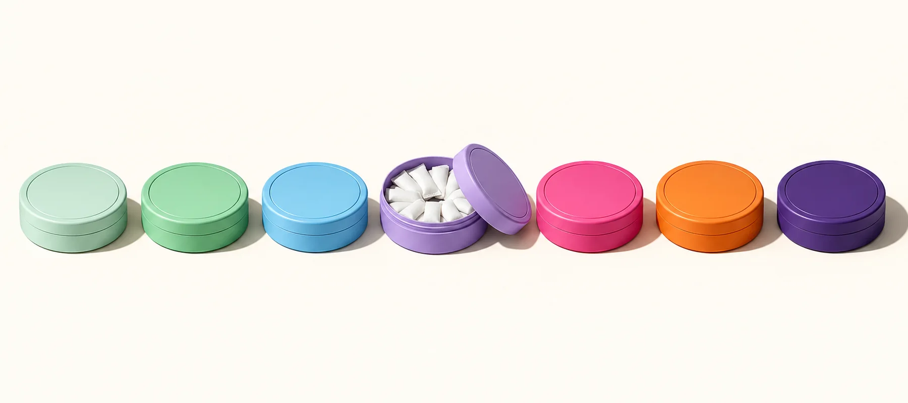 Row of seven nicotine pouch tins from pale to bold colours, one open showing white pouches